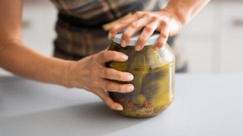 Woman taking the lid off a jar of pickles, from Shelf Cooking