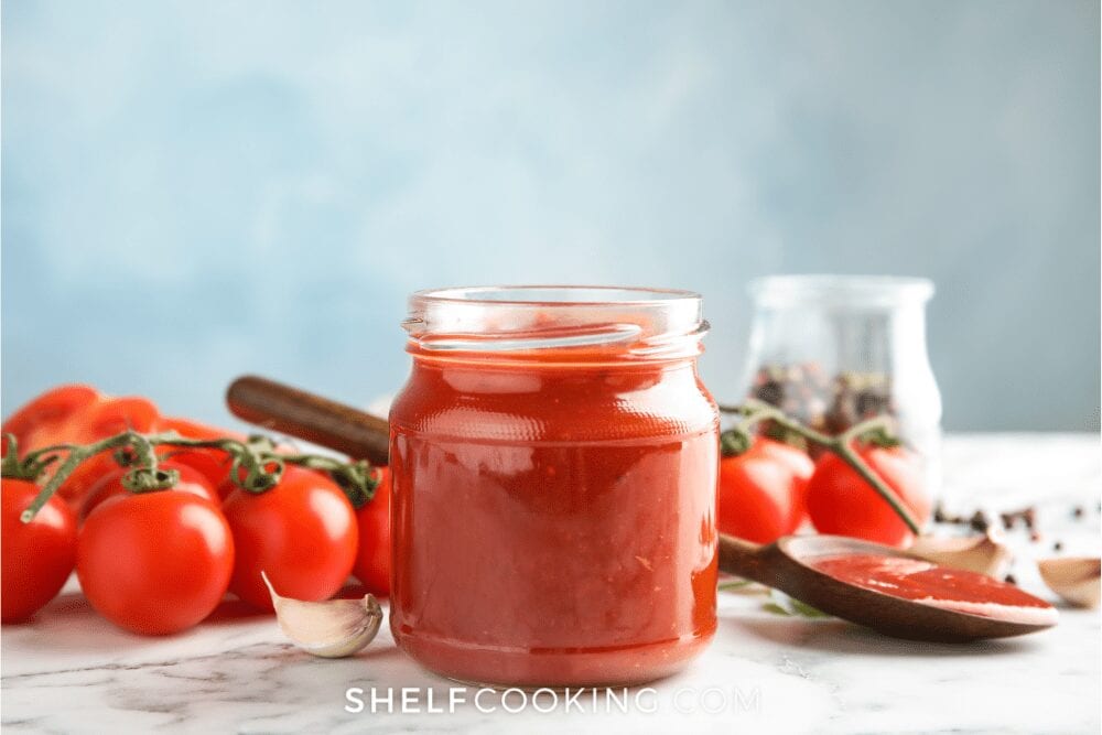 Tomato paste in a jar next to tomatoes, garlic, and peppercorns, from Shelf Cooking