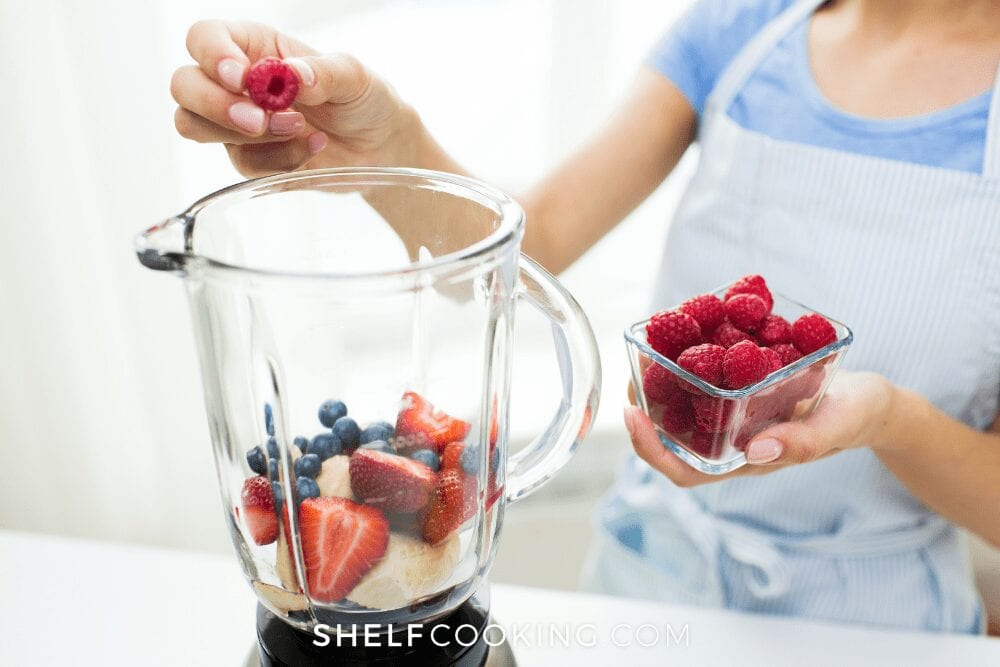 close up of woman putting colorful berries into a glass blender jar, from Shelf Cooking