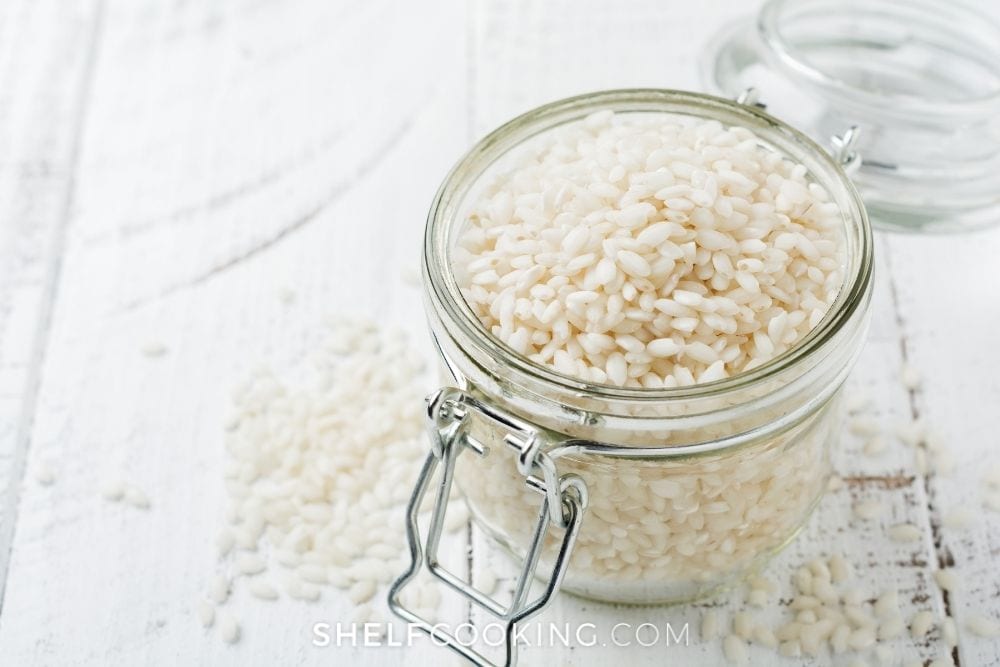 Rice grains in a jar on a wooden table from Shelf Cooking. 