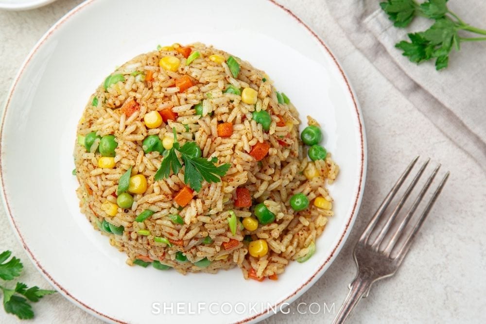 Oven-baked rice on a white plate with vegetables mixed in from Shelf Cooking. 