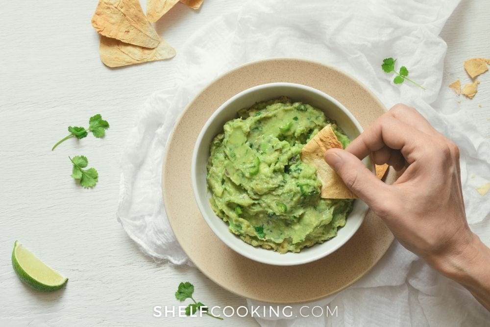 dipping a chip in homemade guacamole, from Shelf Cooking