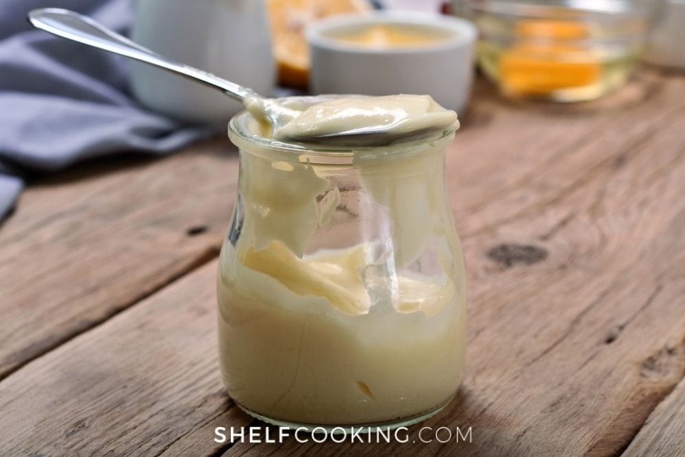 Homemade mayonnaise in a jar with a spoon from Shelf Cooking. 