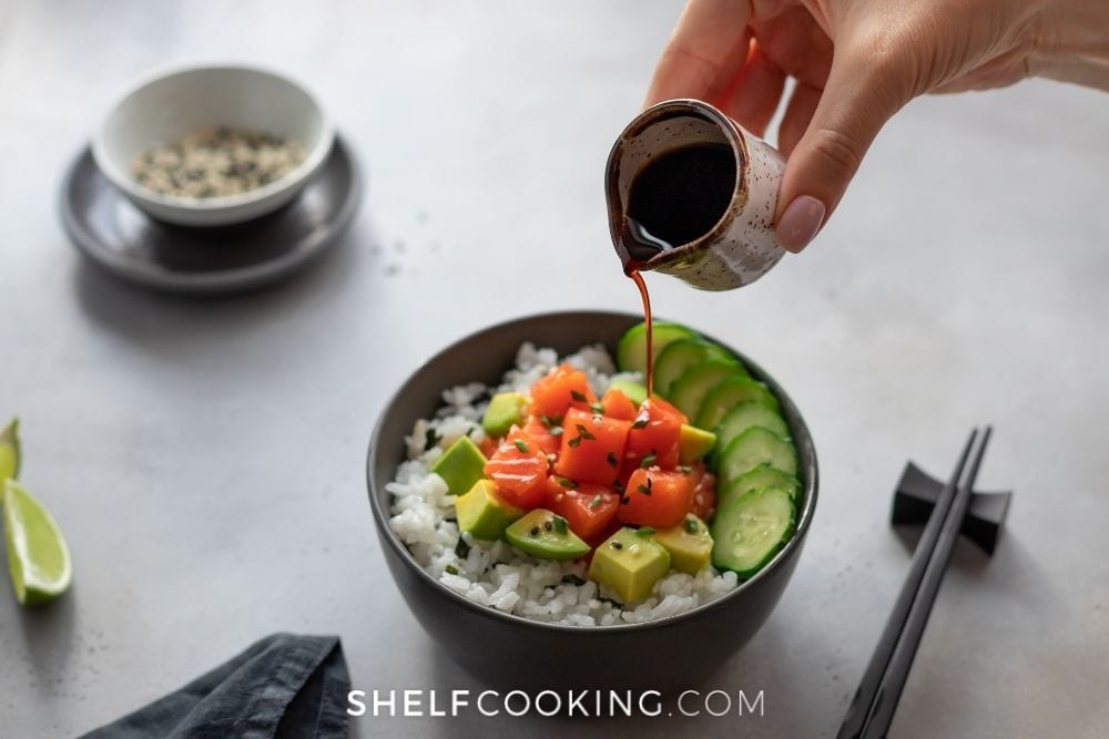 Hand pouring soy sauce on a poke bowl from Shelf Cooking. 