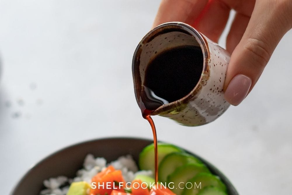 Hand pouring soy sauce into bowl from Shelf Cooking. 