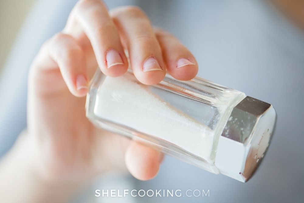 Hand holding a salt shaker from Shelf Cooking. 