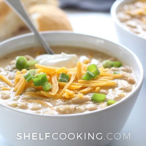 White chicken chili recipe in a bowl with a spoon from Shelf Cooking.