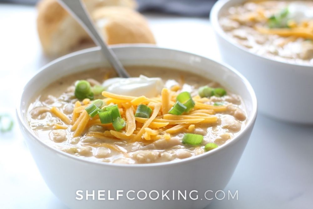 White chicken chili recipe in a bowl with a spoon from Shelf Cooking. 