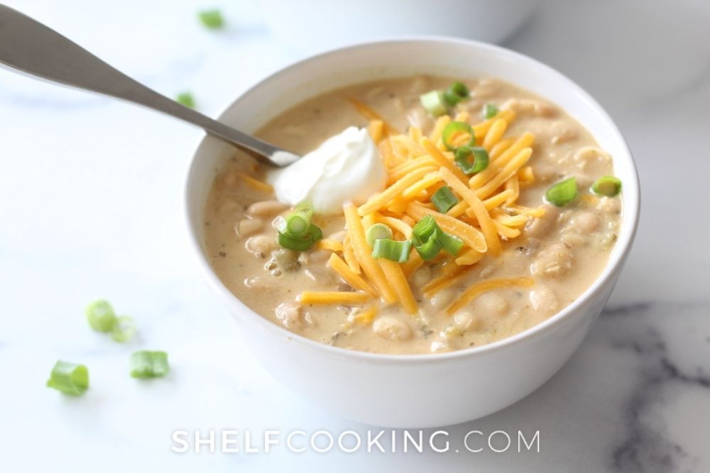 White chicken chili in a bowl with sour cream and cheese from Shelf Cooking. 