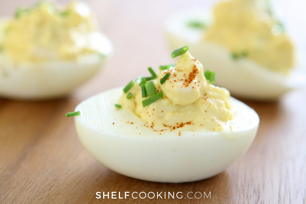 Close image of deviled eggs on a wooden table, with diced chives as garnish on top. - Shelf Cooking