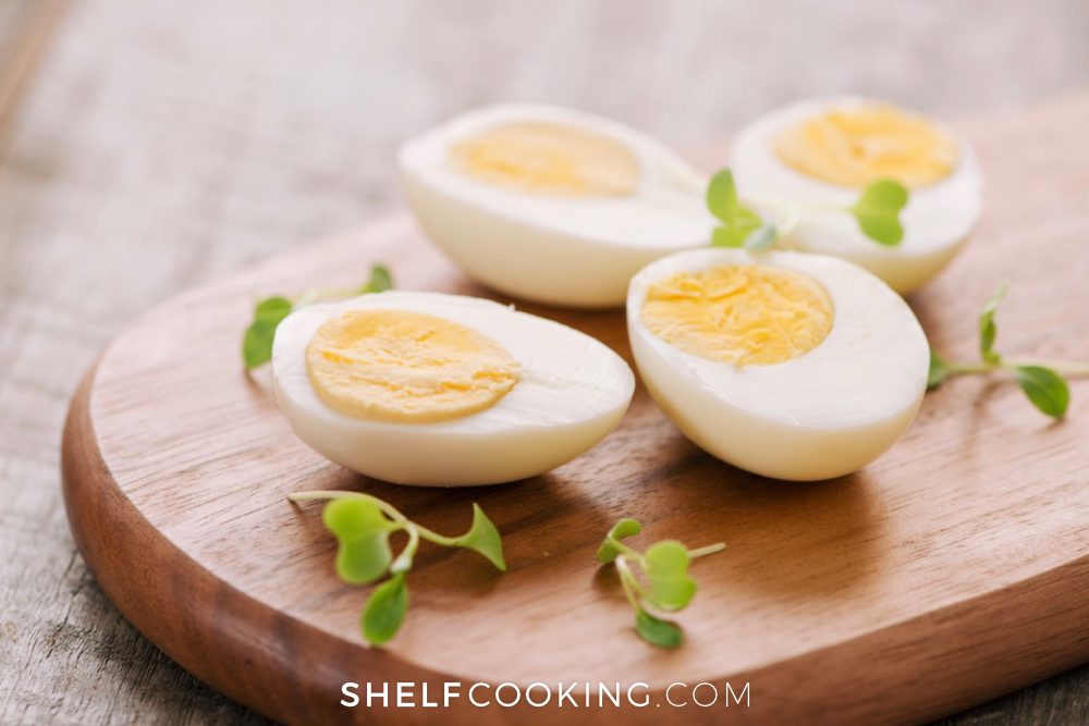 Halved hard boiled eggs on a wood cutting board with small green leaves as garnish - Shelf Cooking