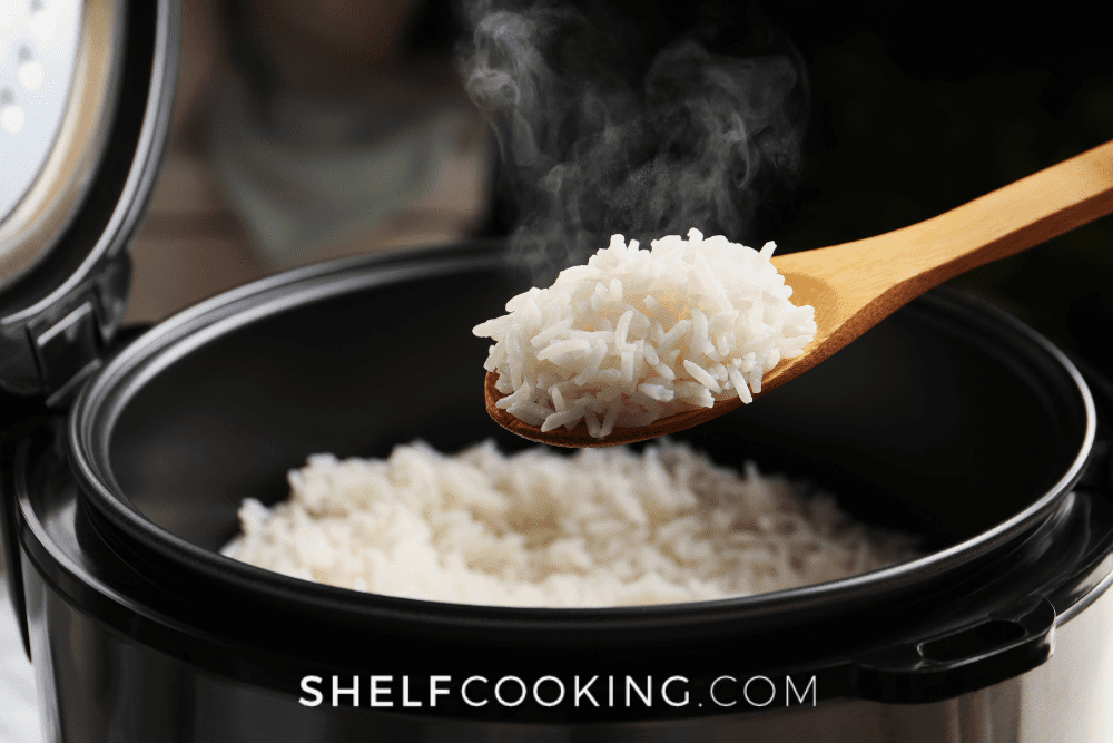 Image of a pressure cooker with cooked white rice. A wooden spoon hovers above holding a scoop. - Shelf Cooking