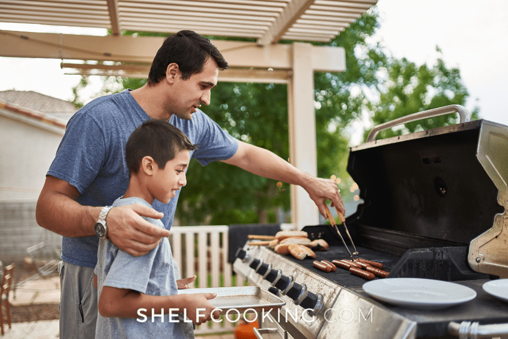 Image of a father and son at a bbq grill. The father is picking up hot dogs with tongs while the son is holding a plate. - Shelf Cooking
