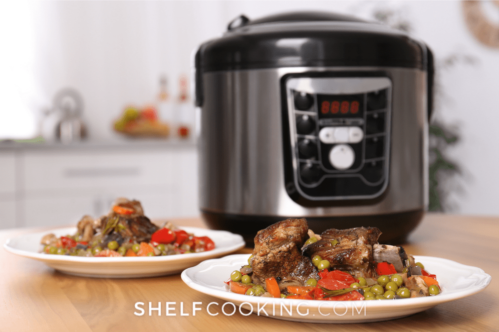 Image of two plates of meat and veggies on white plates in the foreground. In the background is a pressure cooker as a way to save money in the kitchen. - Shelf Cooking