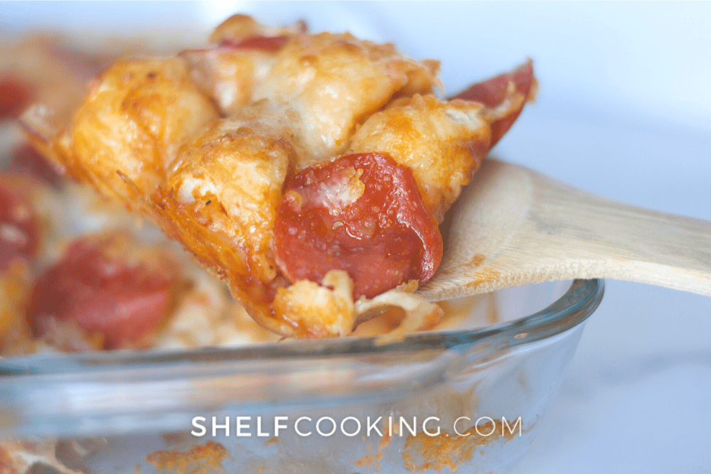 Image of a wooden spoon holding a piece of pizza casserole with cheese and pepperoni on top. - Shelf Cooking