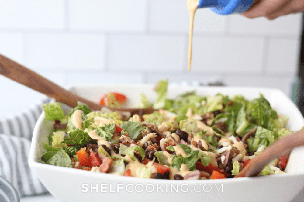 Image of a large Cowboy Salad with dressing being poured on it. - Shelf Cooking