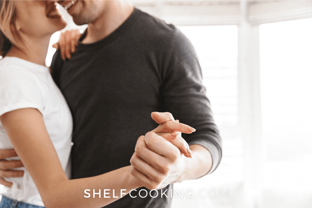 A man and woman are dancing together. The camera is focused on their clasped hands and they appear to be smiling. - Shelf Cooking