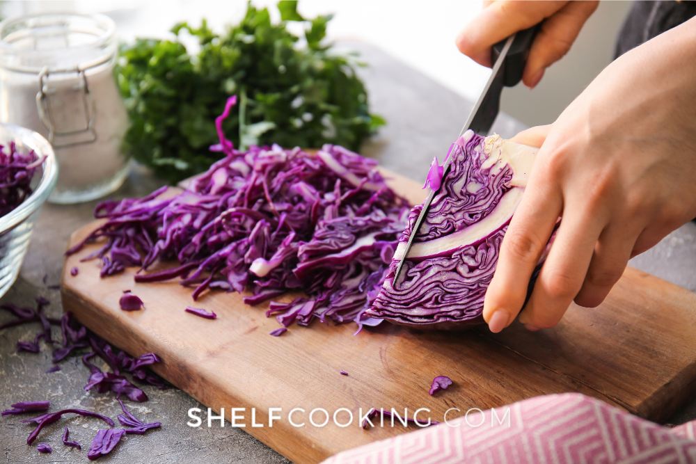 Image of a head of purple cabbage being sliced on a wooden cutting board. - Shelf Cooking